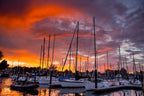 Sailboat masts in a harbor under a red and orange sunset sky
