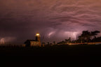 Lightning behind a lighthouse under a stormy purple sky