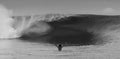 A black and white photo of a swimmer with arms raised in front of a huge wave