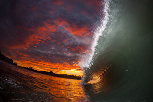 A tunnel of water lit by a fiery orange and red sunset sky