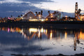 A seaside amusement park with a roller coaster and Ferris wheel reflected in still water at dusk