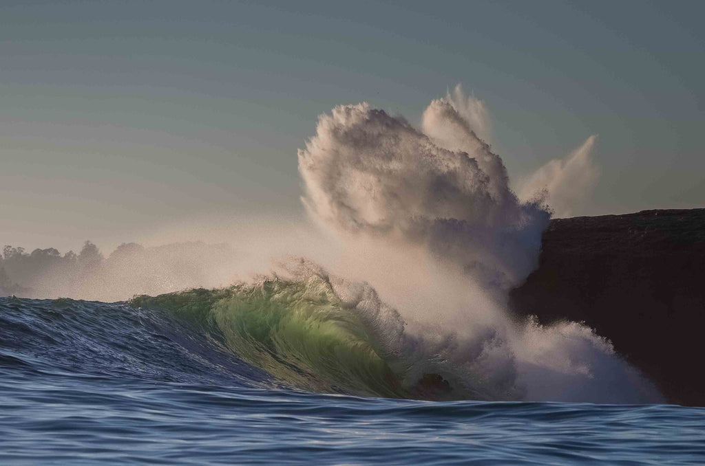A wave exploding into a cloud of spray against a dark cliff