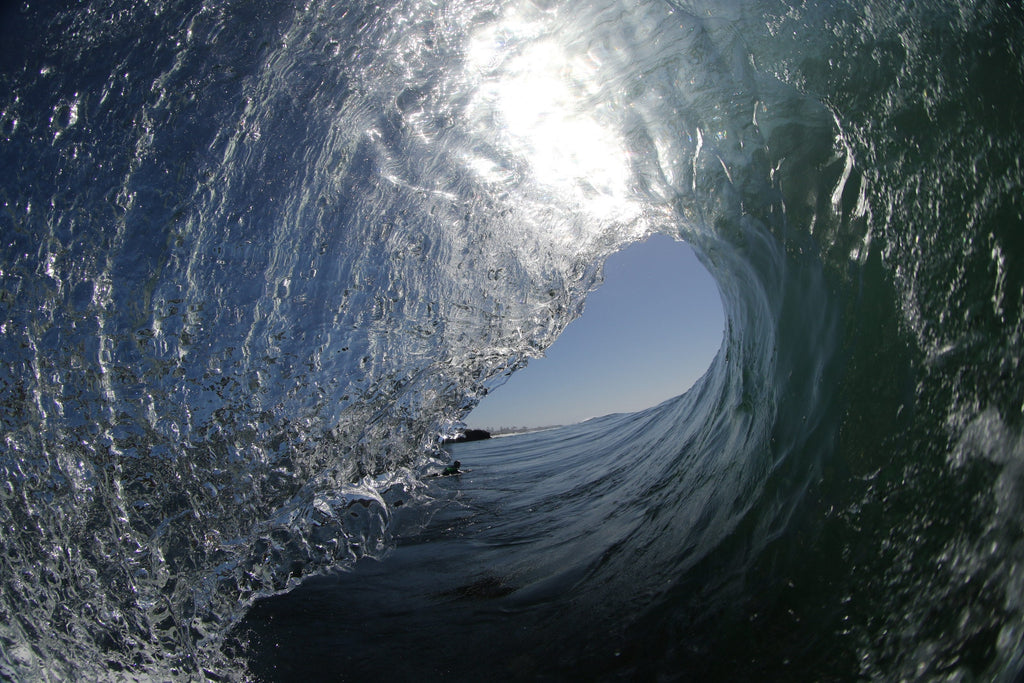 The inside of a glassy wave with a bright blue opening and silver textured water