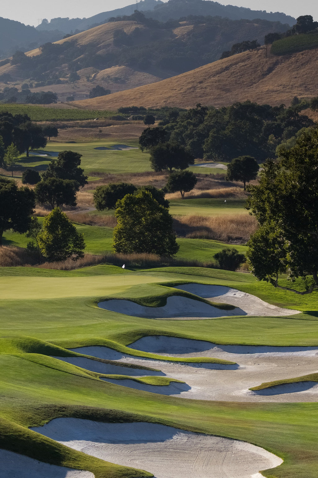 A golf course fairway winding through green hills with white sand bunkers
