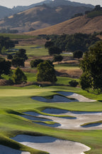 A golf course fairway winding through green hills with white sand bunkers