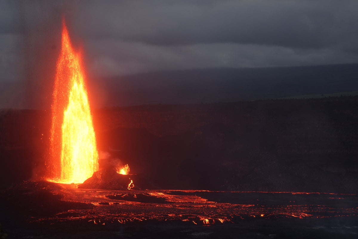 A fountain of lava shooting up from a dark crater under a stormy sky