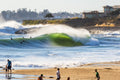 A green wave breaking close to a beach with people walking on the sand