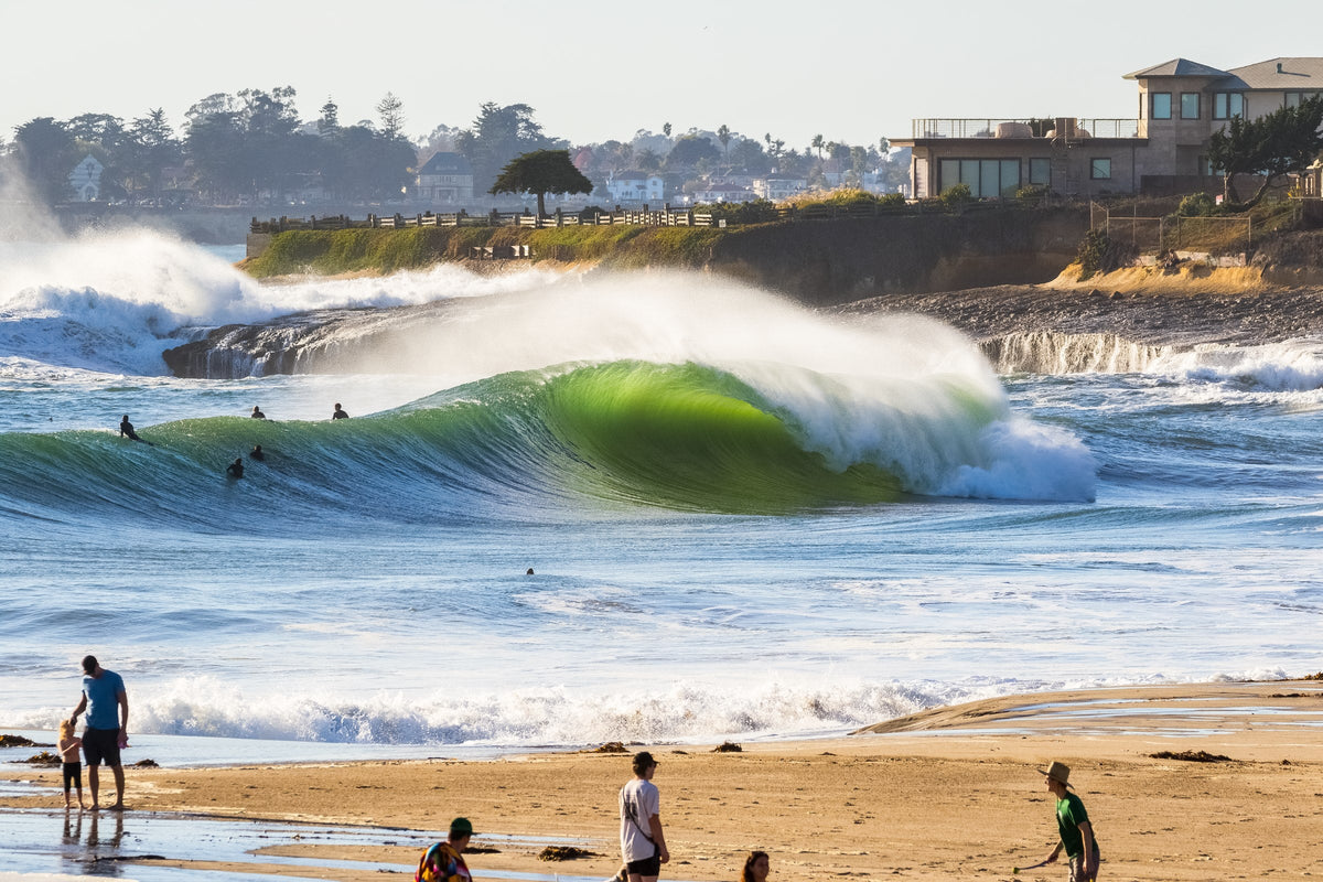 A green wave breaking close to a beach with people walking on the sand
