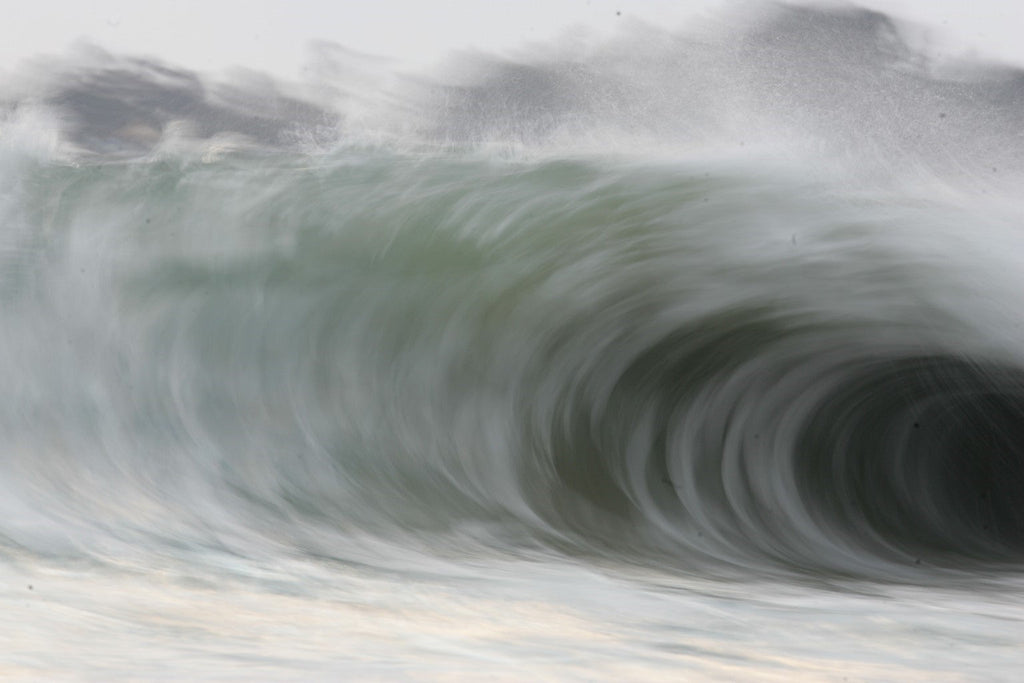 A huge curling wave seen close with soft grey and green tones