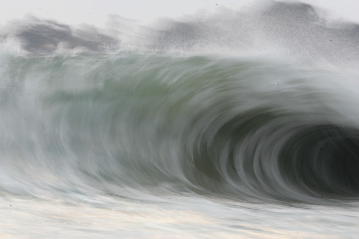 A huge curling wave seen close with soft grey and green tones