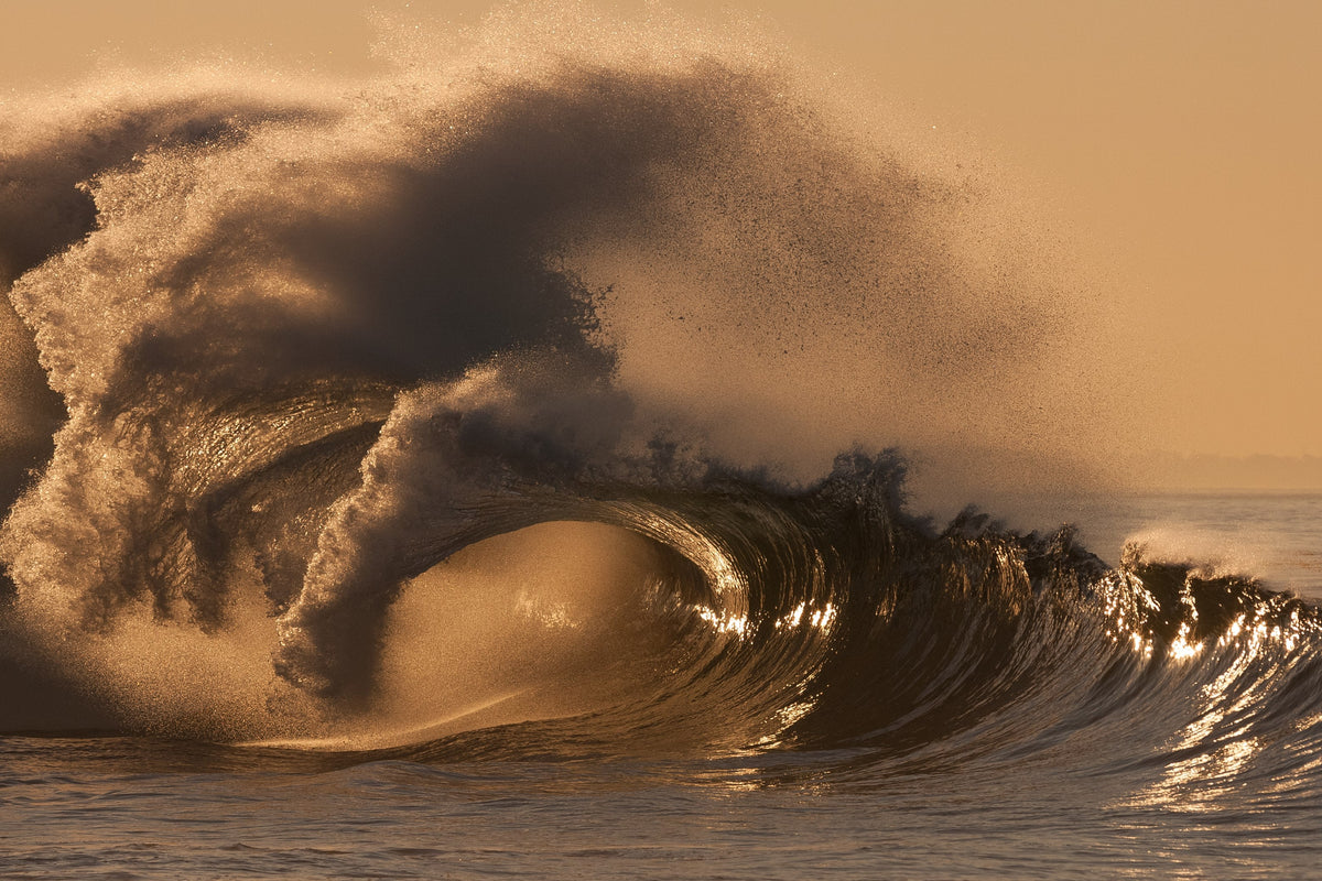 A wave exploding into golden spray at sunrise