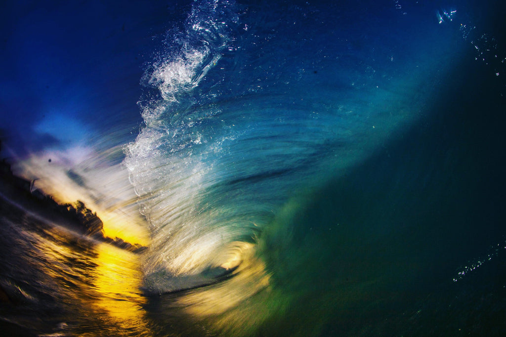 Inside a dark blue wave with golden sunset light at the opening