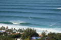 An aerial view of long lines of waves rolling toward a palm-lined beach