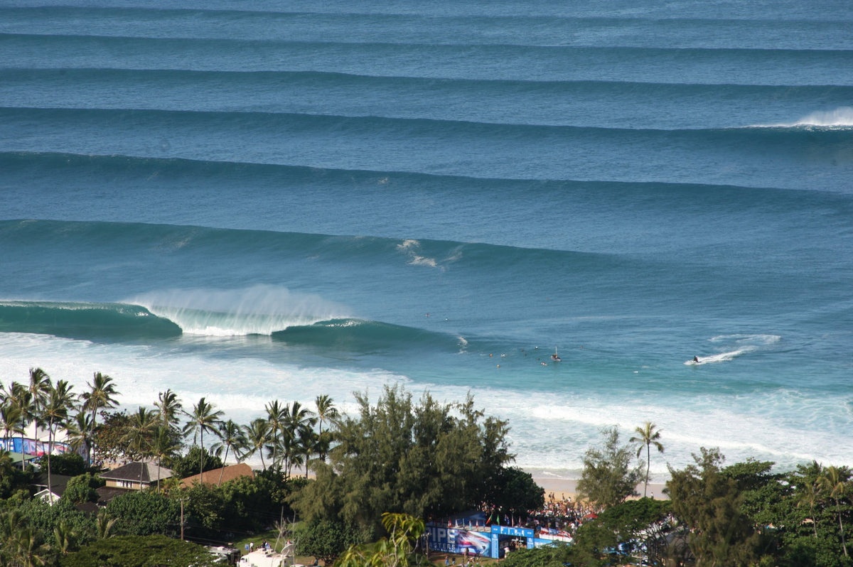An aerial view of long lines of waves rolling toward a palm-lined beach