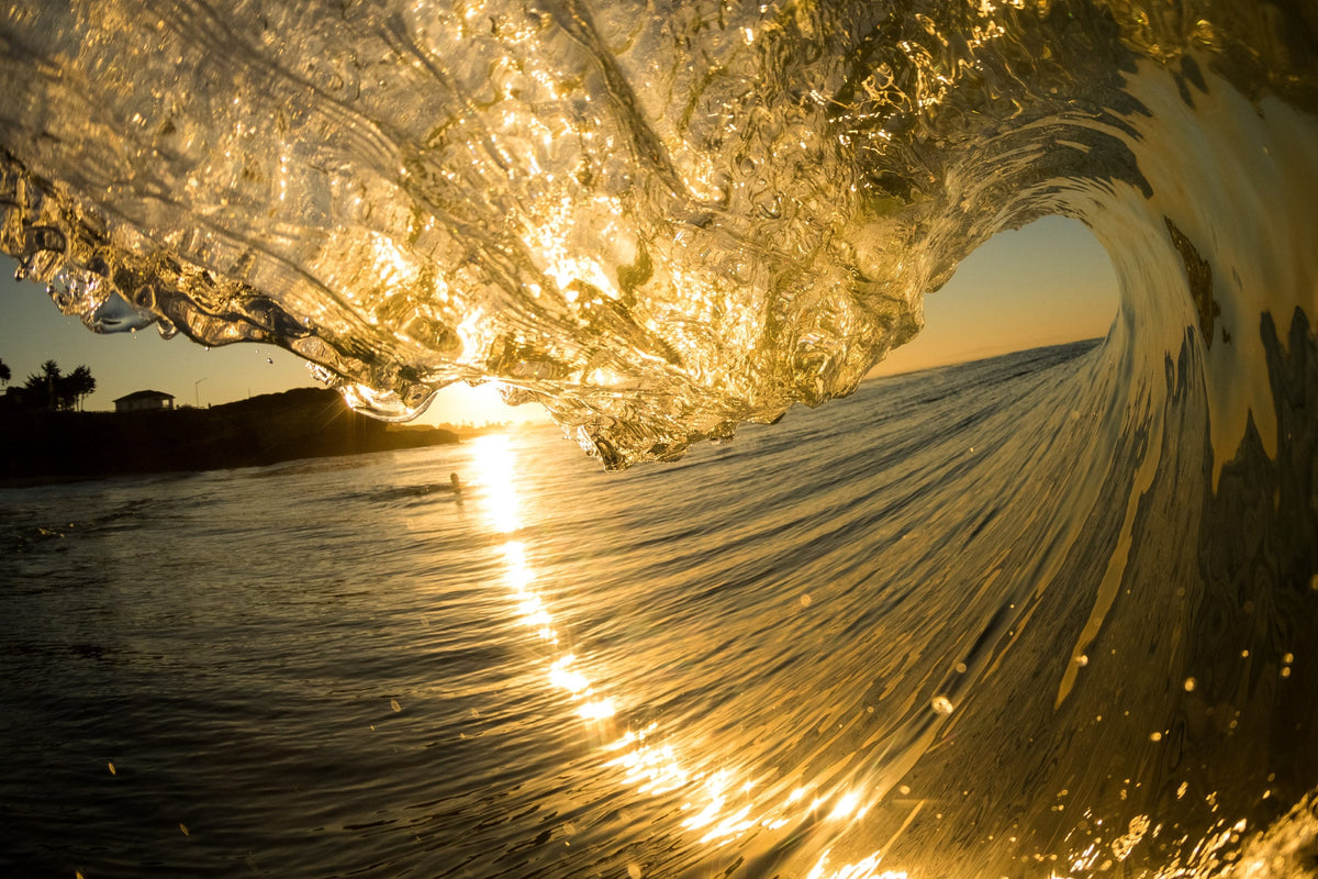 A wave curling in gold light with glittering water streaming down its face