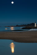 A full moon over a lighthouse and its reflection at dusk