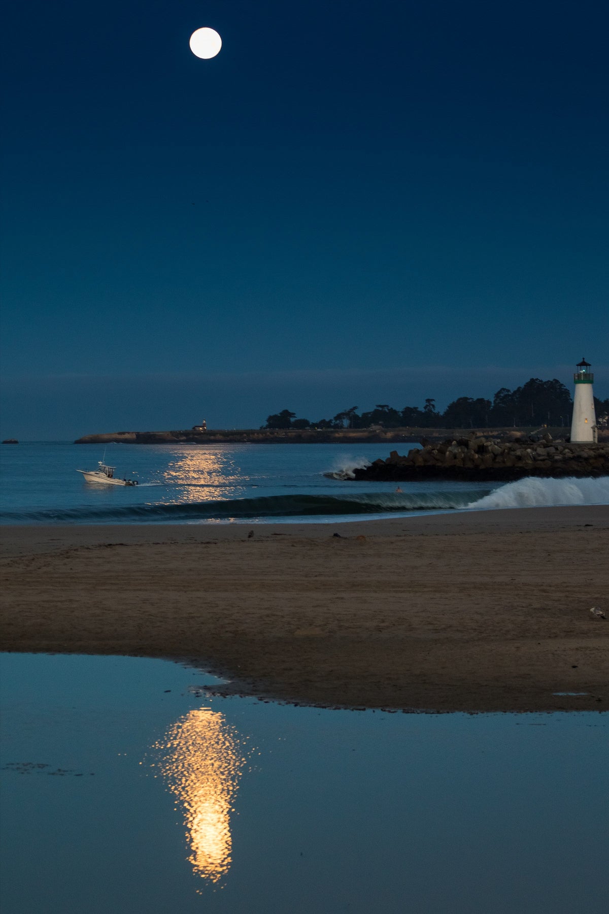 A full moon over a lighthouse and its reflection at dusk