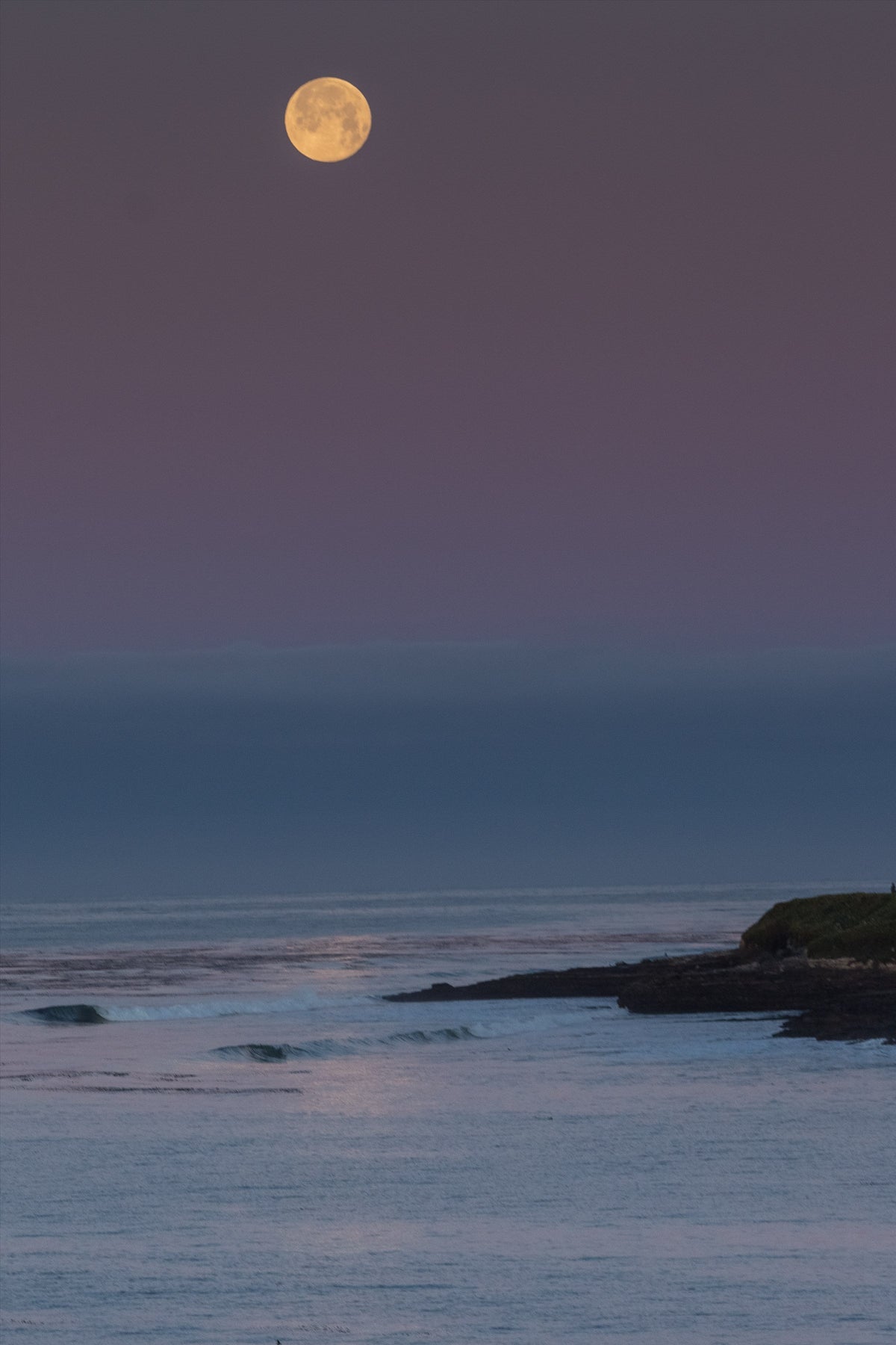 A moon rising over a calm sea at dusk