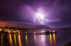 Lightning striking over a lit pier and harbor at night