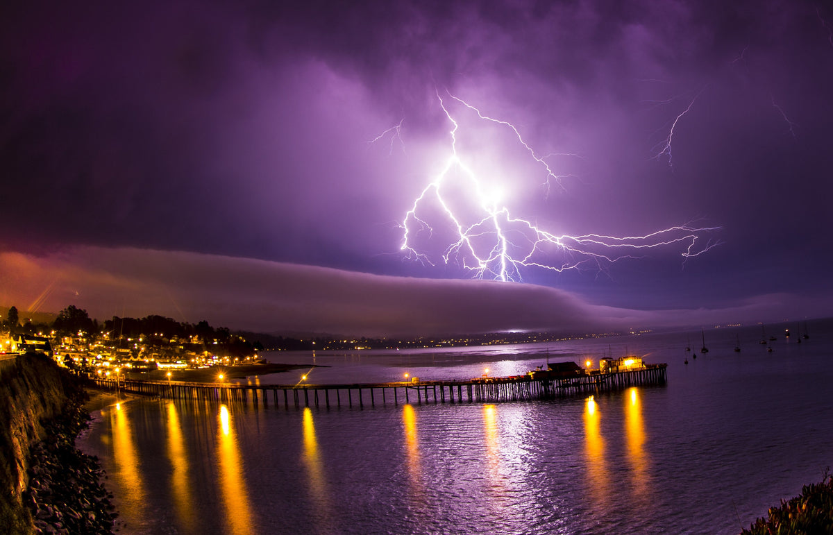 Lightning striking over a lit pier and harbor at night