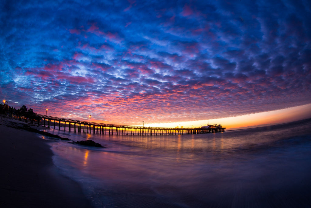 A fisheye view of a long pier under a sky of blue and pink clouds at sunset