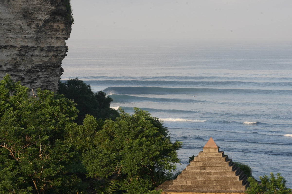 Long lines of swell marching past a rocky headland with a stone pyramid