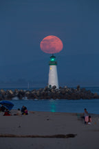 A red moon rising directly above a lighthouse at dusk
