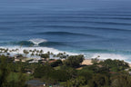 Long lines of swell approaching a palm-lined beach from above