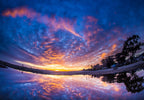 A sunset sky of purple and orange clouds reflected in a still puddle on the beach