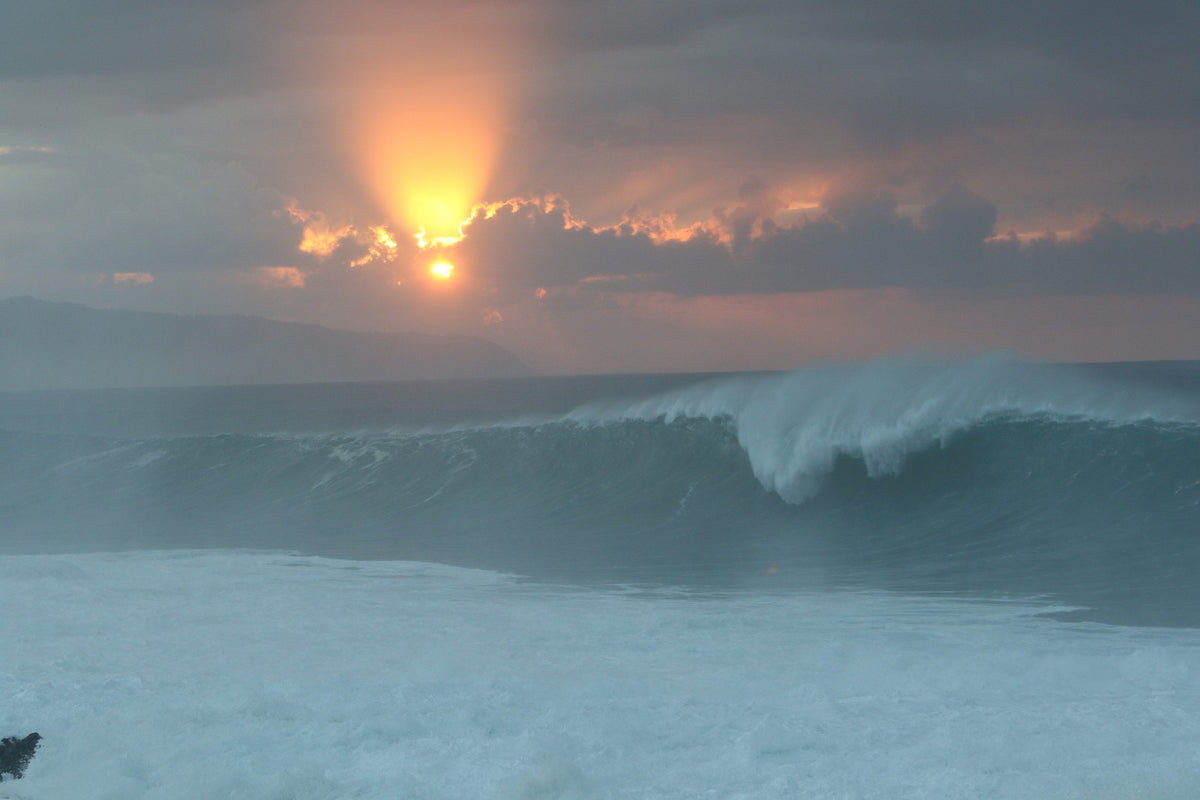 A glowing sun behind clouds above a peeling blue wave