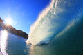 A bright blue wave lit by a sunburst over a rocky point