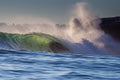 A heavy wave breaking next to a cliff with a plume of spray
