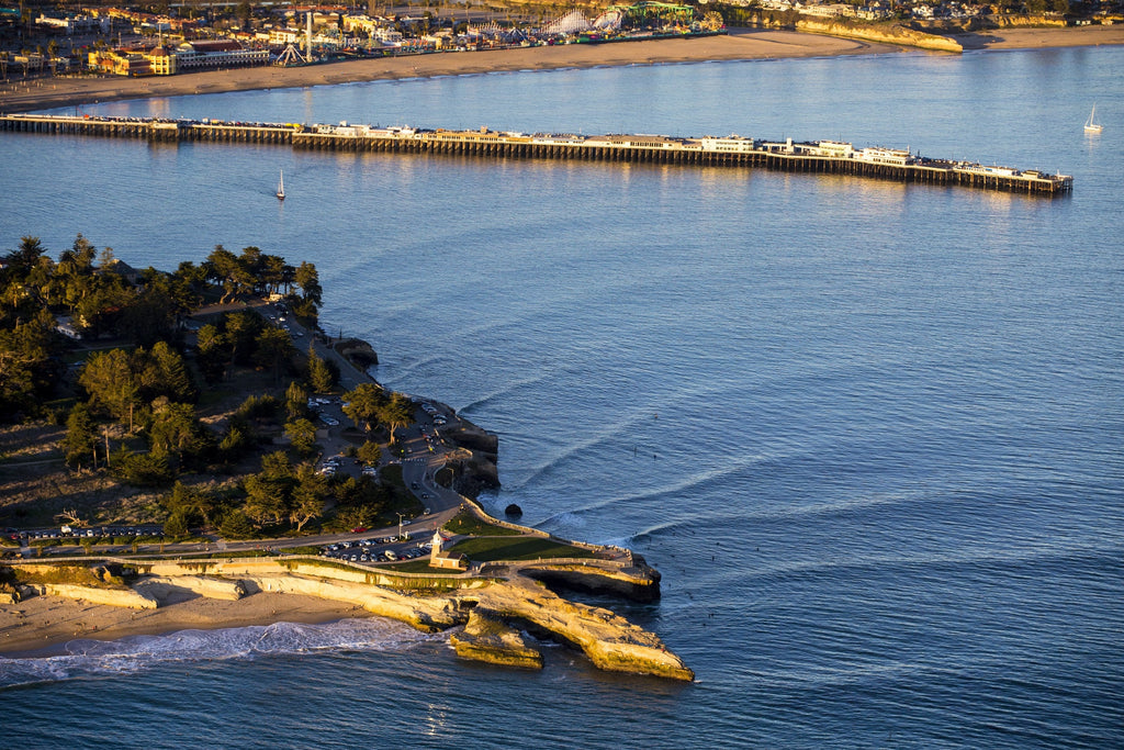 An aerial view of a long wharf and rocky point in blue water at golden hour