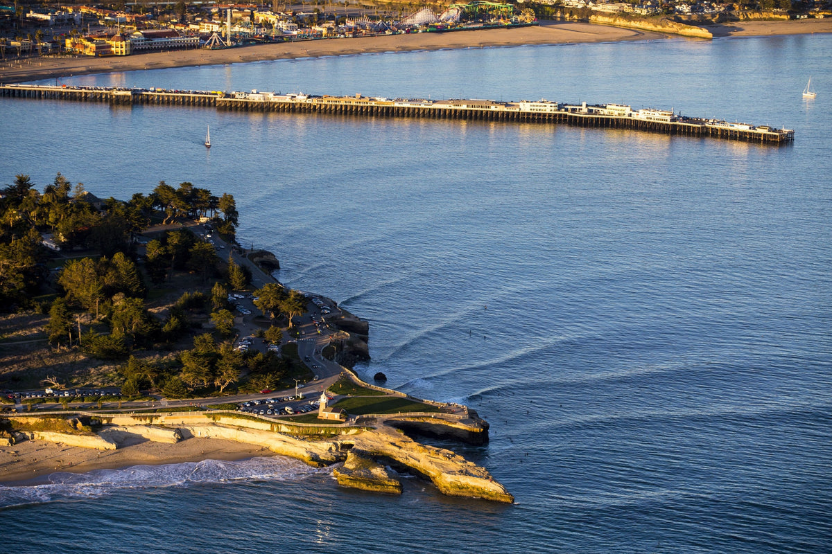 An aerial view of a long wharf and rocky point in blue water at golden hour