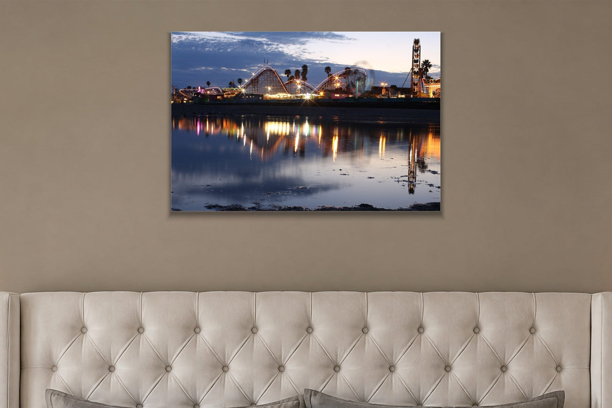 A seaside amusement park with a roller coaster and Ferris wheel reflected in still water at dusk shown large on the wall of a lived-in room