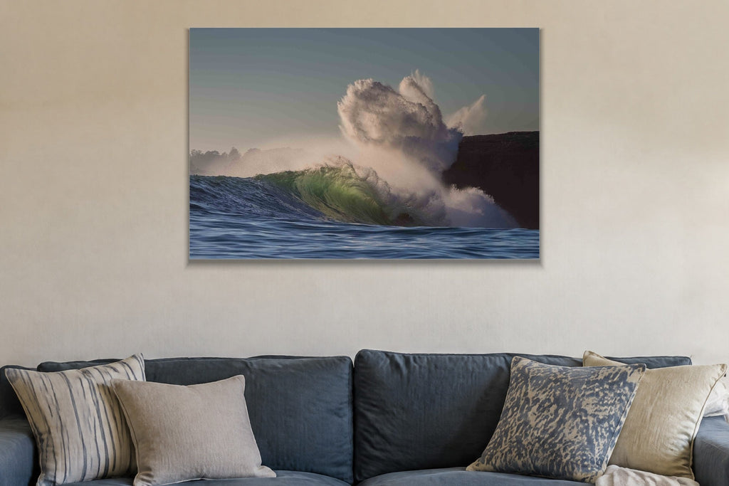 A wave exploding into a cloud of spray against a dark cliff shown large on the wall of a lived-in room