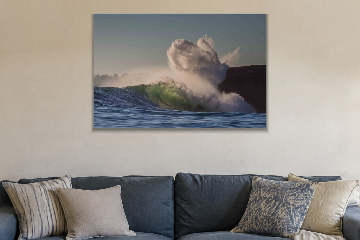 A wave exploding into a cloud of spray against a dark cliff shown large on the wall of a lived-in room