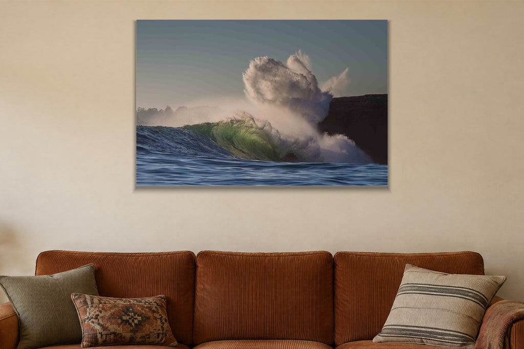 A wave exploding into a cloud of spray against a dark cliff shown large on the wall of a lived-in room