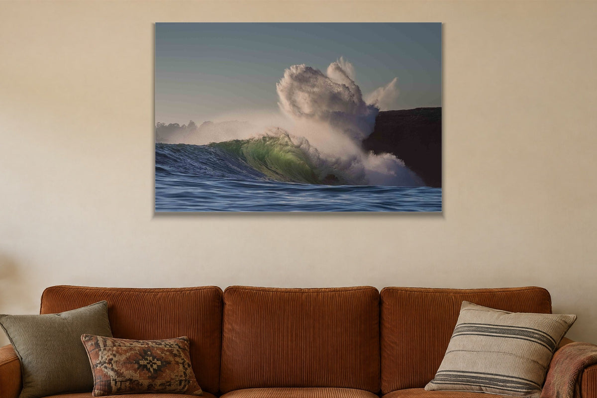 A wave exploding into a cloud of spray against a dark cliff shown large on the wall of a lived-in room