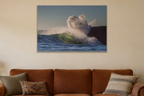 A wave exploding into a cloud of spray against a dark cliff shown large on the wall of a lived-in room