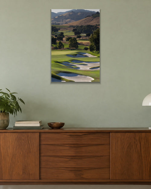 A golf course fairway winding through green hills with white sand bunkers shown large on the wall of a lived-in room