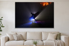 A silhouetted figure carrying a surfboard through beams of blue light on a dark beach with a warm glow on the rocks behind shown large on the wall of a lived-in room