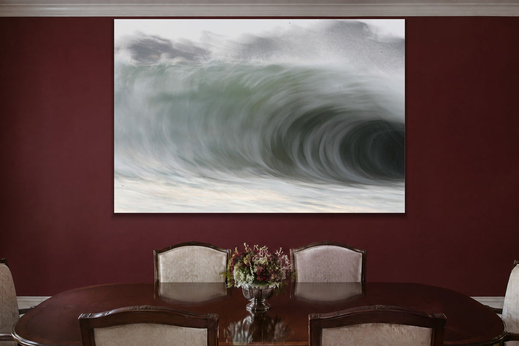 A huge curling wave seen close with soft grey and green tones shown large on the wall of a lived-in room
