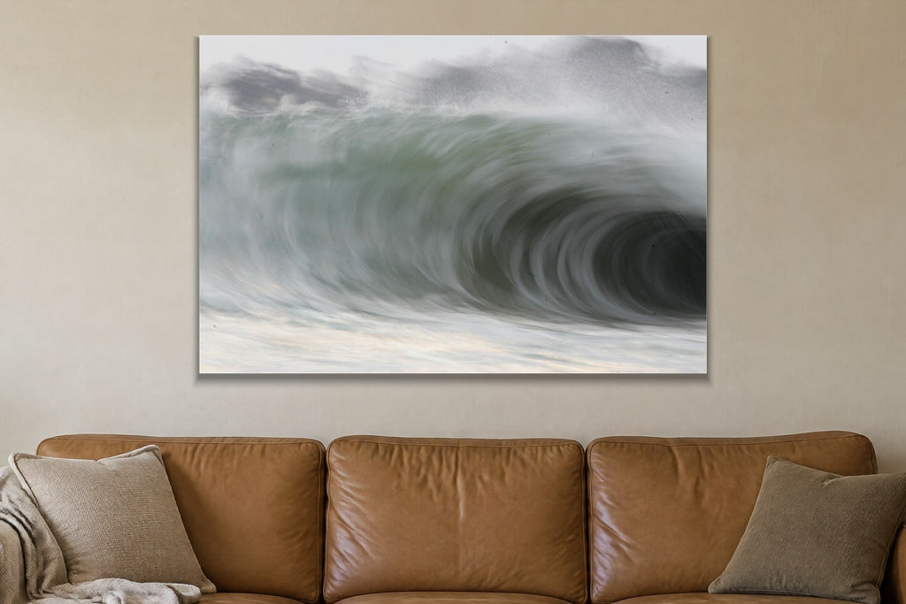 A huge curling wave seen close with soft grey and green tones shown large on the wall of a lived-in room