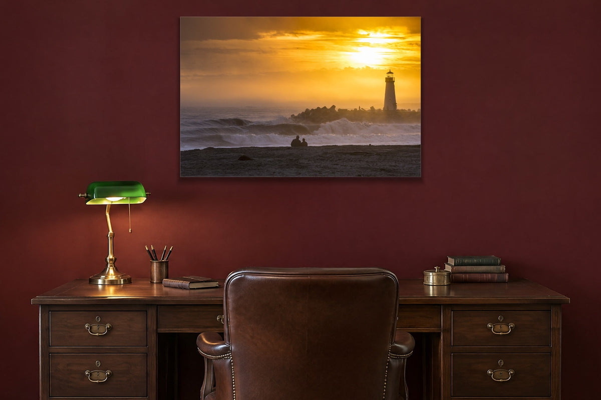 A lighthouse on a breakwater under a golden sunset with a couple watching from the shore shown large on the wall of a lived-in room