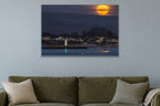 A huge orange full moon rising above a harbor town with a lighthouse and a sailboat shown large on the wall of a lived-in room