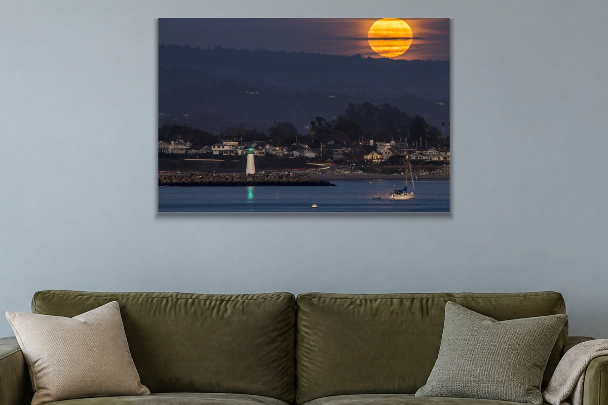 A huge orange full moon rising above a harbor town with a lighthouse and a sailboat shown large on the wall of a lived-in room