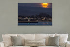 A huge orange full moon rising above a harbor town with a lighthouse and a sailboat shown large on the wall of a lived-in room