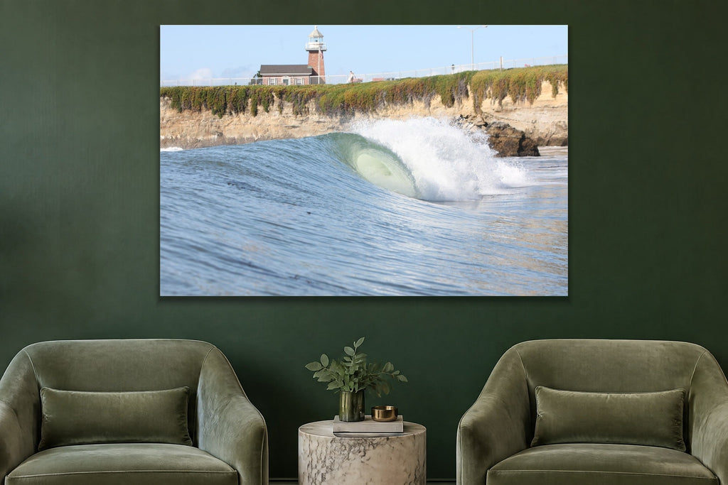 A glassy wave breaking along a cliff below a brick lighthouse shown large on the wall of a lived-in room