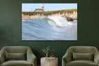 A glassy wave breaking along a cliff below a brick lighthouse shown large on the wall of a lived-in room